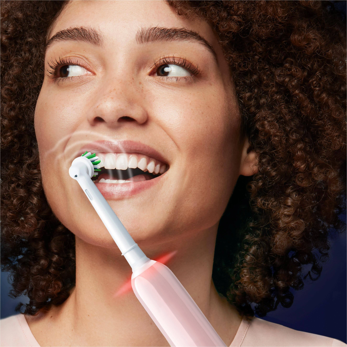 Mujer cepillándose los dientes con un cepillo de dientes eléctrico rosa. Sale vapor de su boca, mostrando higiene bucal.