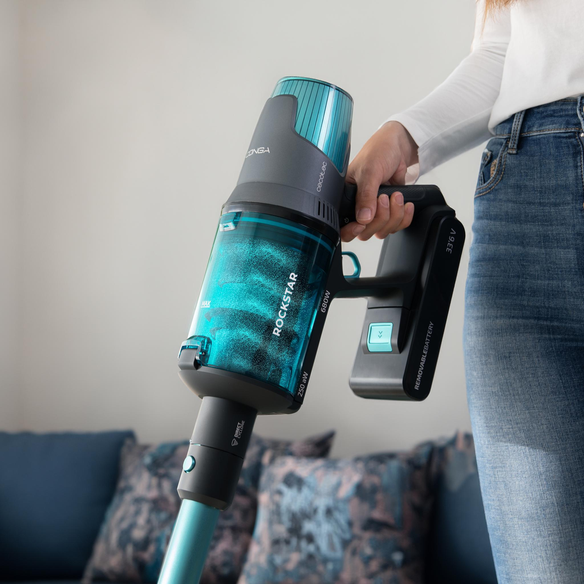 Una donna tiene in mano un aspirapolvere senza fili blu e grigio. È in uso.
