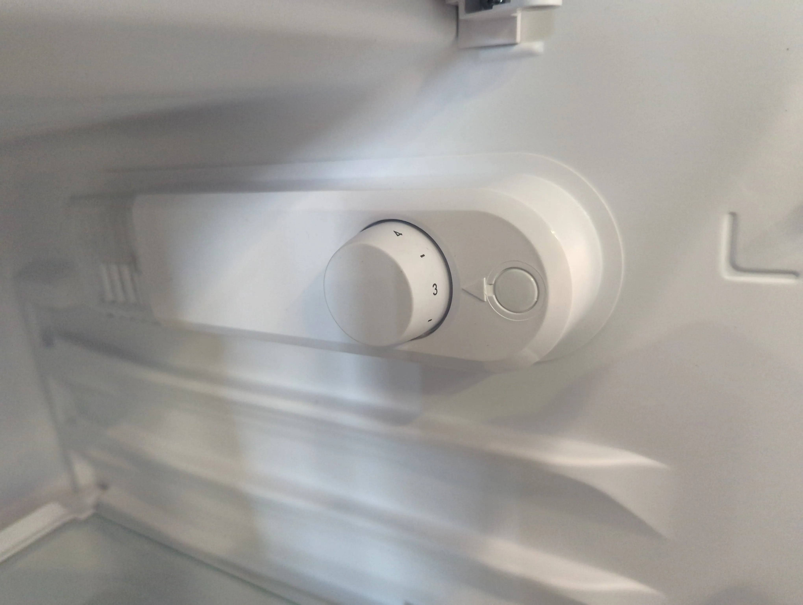 Interior de refrigerador. Paredes blancas, un dial de temperatura y una lámpara.