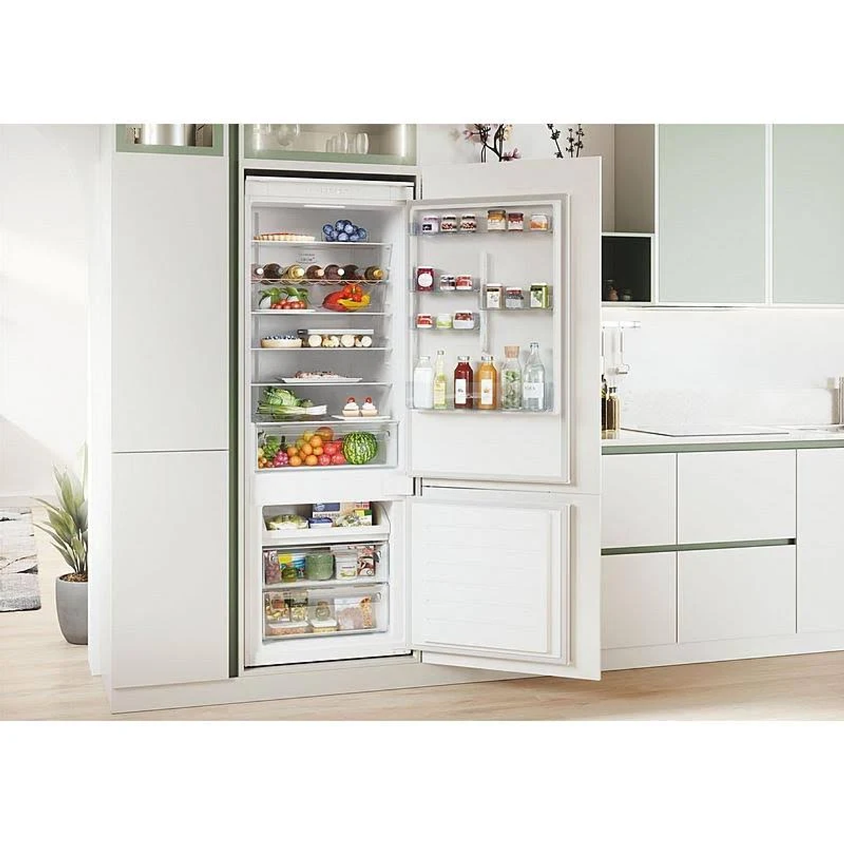 Biała lodówka z otwartymi drzwiami, pełna artykułów spożywczych. W tle kuchnia.