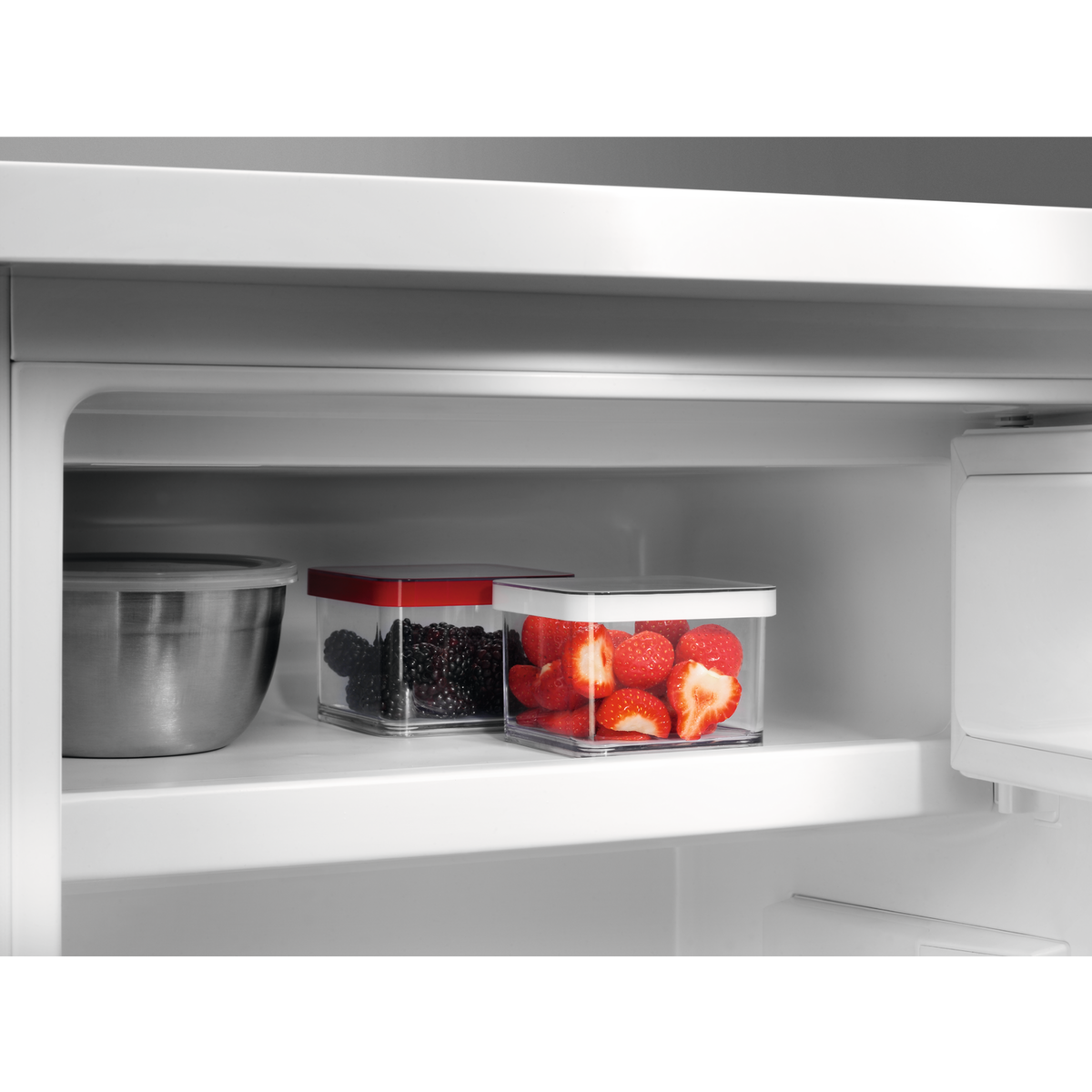 All'interno di un frigorifero, due contenitori trasparenti contengono bacche e fragole.