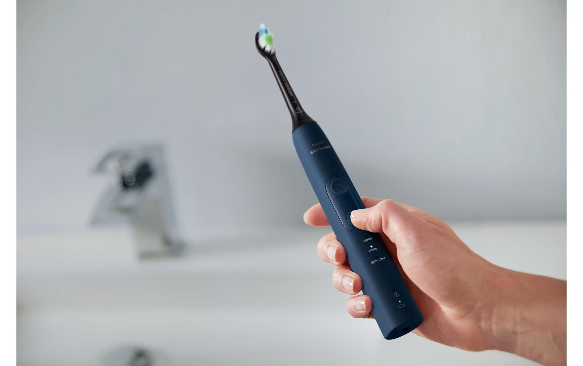 Mano che tiene uno spazzolino elettrico blu vicino a un lavandino. Lo spazzolino ha un pulsante.