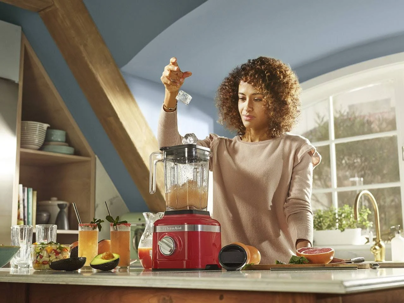 Kobieta dodaje lód do blendera. Czerwony blender na blacie. Kuchnia z belkami.