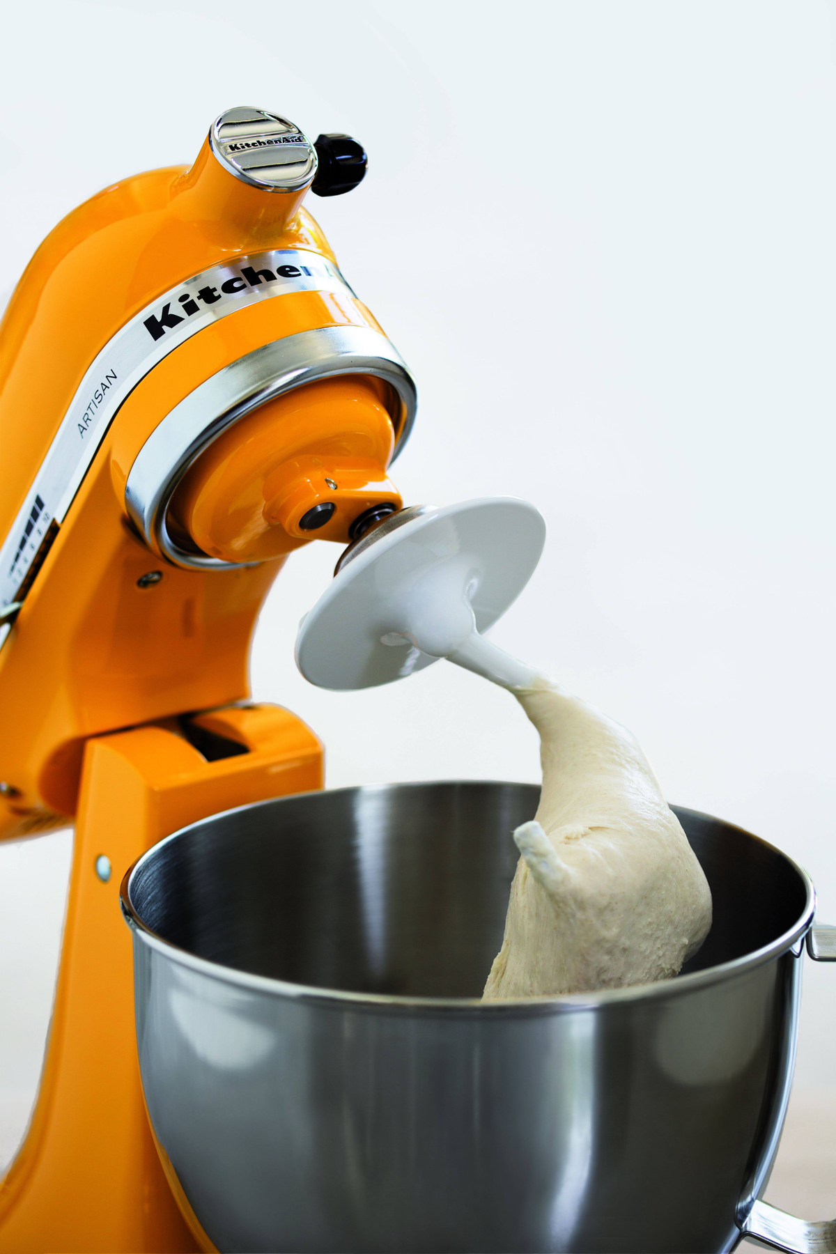 Orangener KitchenAid-Mixer mit Teig am Knethaken, weißer Hintergrund.