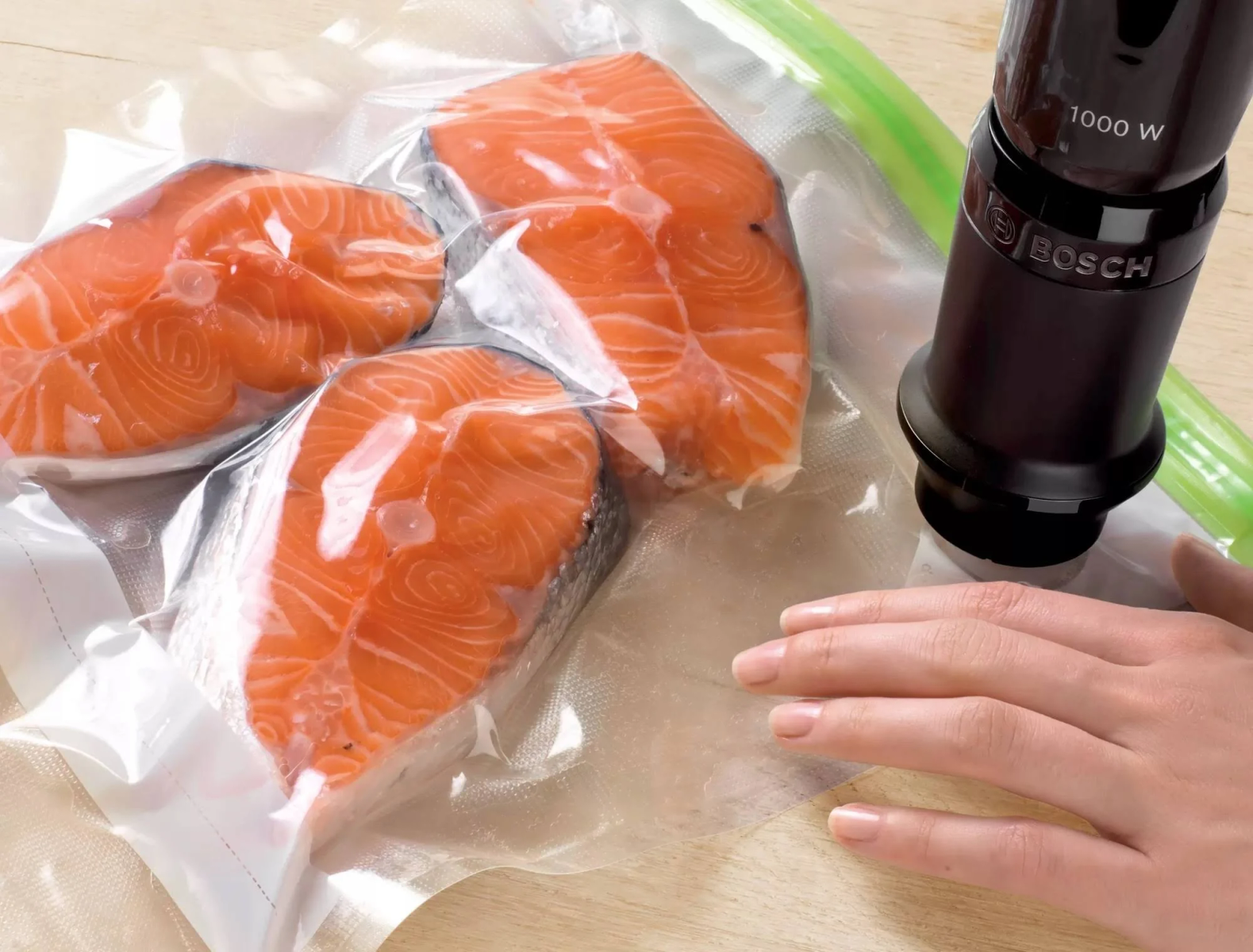 Drei Lachssteaks in Vakuumbeuteln werden mit einer Bosch-Maschine versiegelt. Hand rechts.