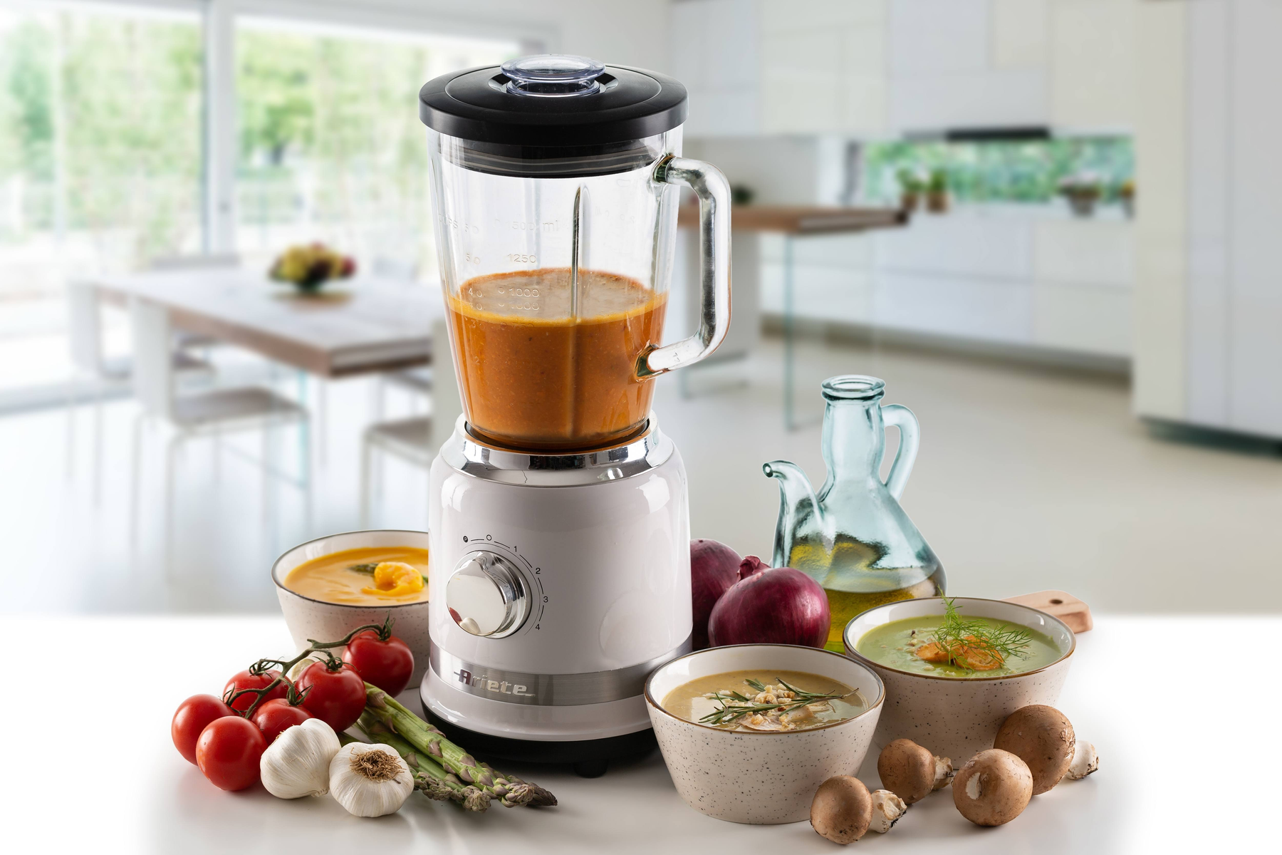 Witte blender met een glazen pot. Ingrediënten voor soep, waaronder tomaten, knoflook en champignons, zijn eromheen gerangschikt.
