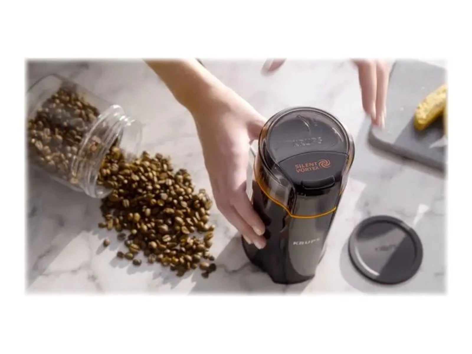 Ziarna kawy są wsypywane do czarnego młynka do kawy KRUPS.