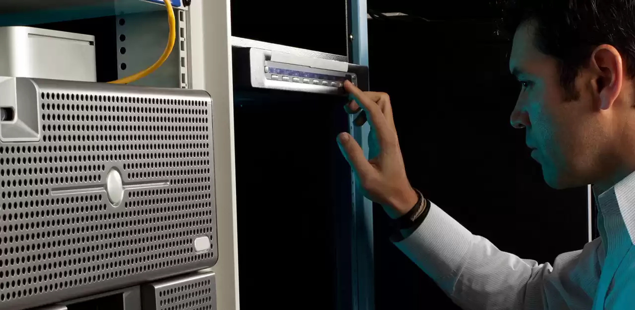 Mężczyzna w białej koszuli dotyka panelu sterowania na szafie serwerowej.