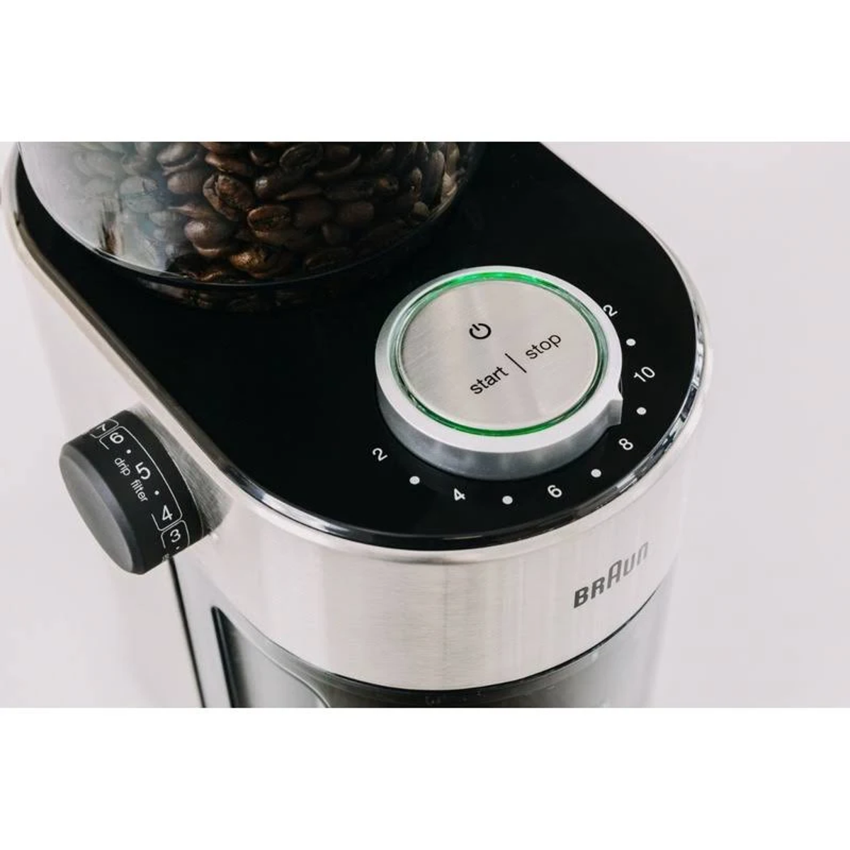 Zbliżenie na młynek do kawy z ziarnami w szklanym pojemniku, przyciskiem zasilania i ustawieniami.