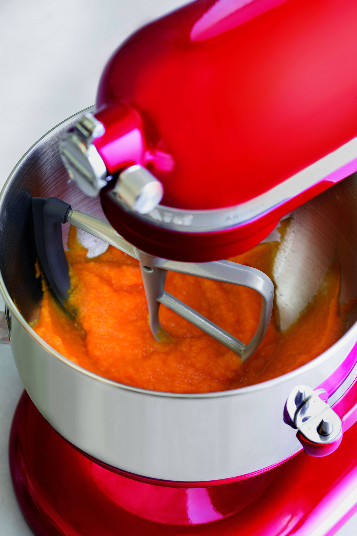 Ein roter Küchenmixer, der eine hellorangefarbene Substanz in einer Edelstahlschüssel verrührt.