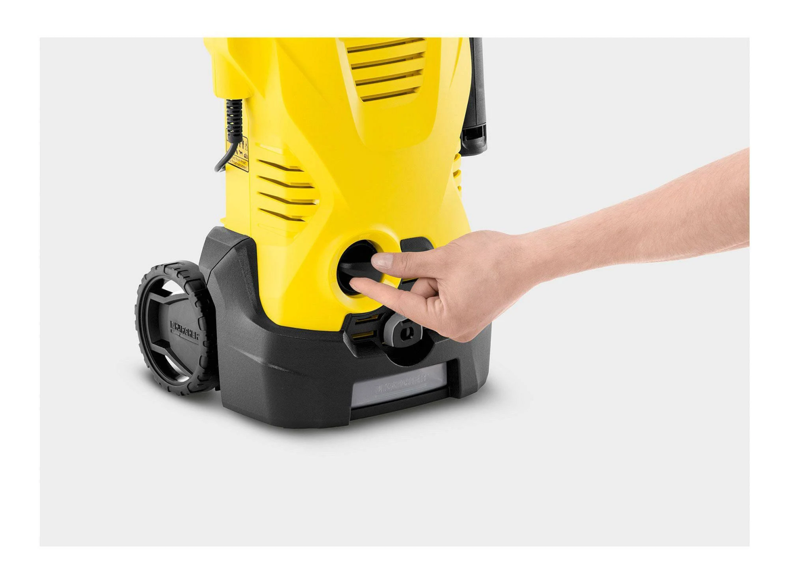 Ręka osoby obsługuje czarny przycisk na żółtej myjce ciśnieniowej.