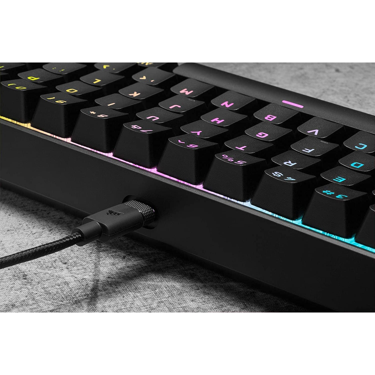Teclado negro con teclas iluminadas, cable enchufado, toma cercana.