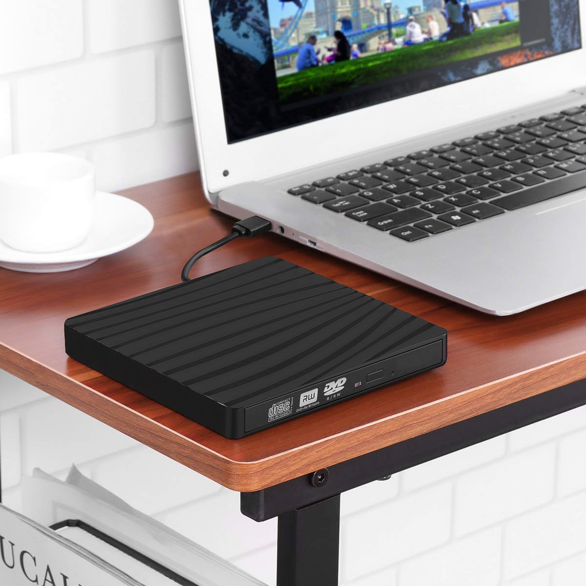 Schwarzes tragbares DVD-Laufwerk, das an einen Laptop angeschlossen ist. Der Laptop ist offen, auf einem Holztisch.