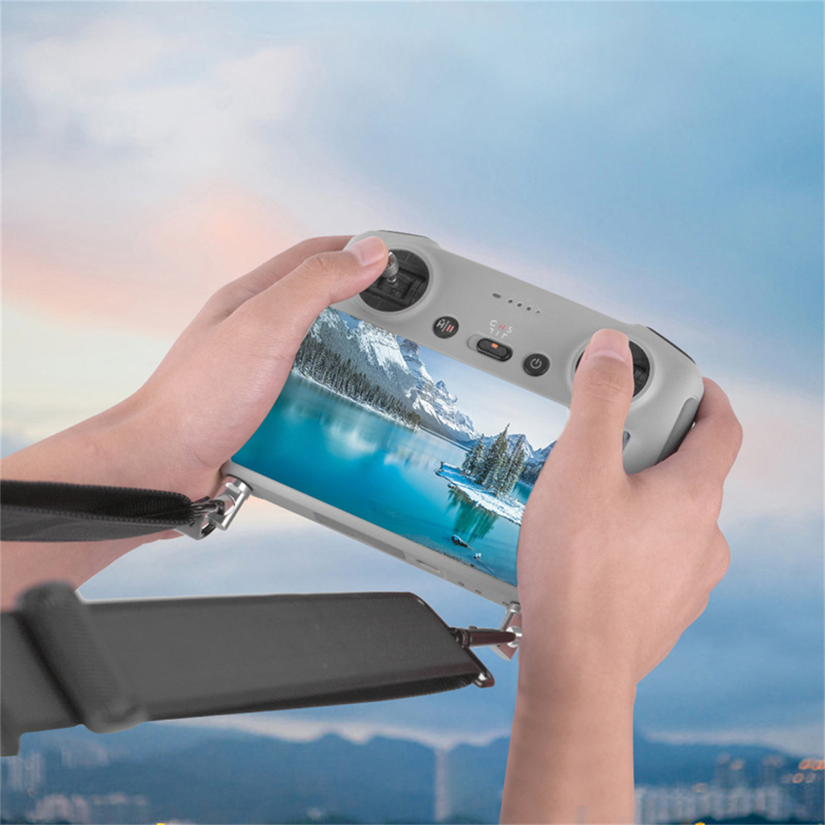Person hält Drohnen-Controller mit Bildschirm, der schneebedeckte Landschaft zeigt. Himmel im Hintergrund.
