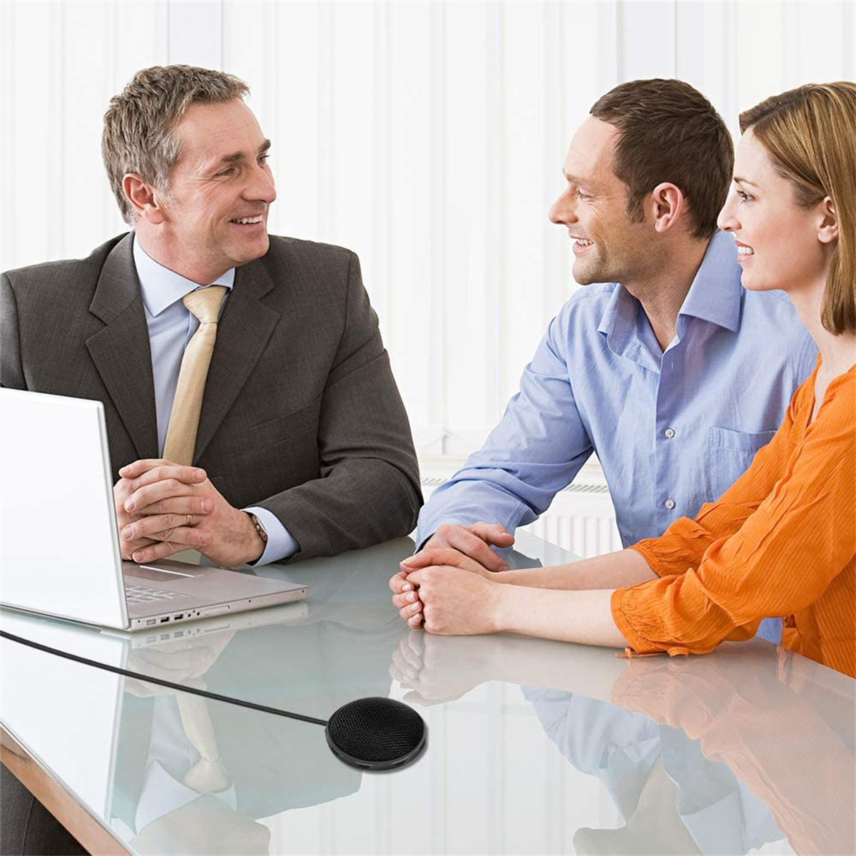 Drei Personen in einem Meeting mit Mikrofon auf dem Tisch, lächelnd, mit hellem Hintergrund.