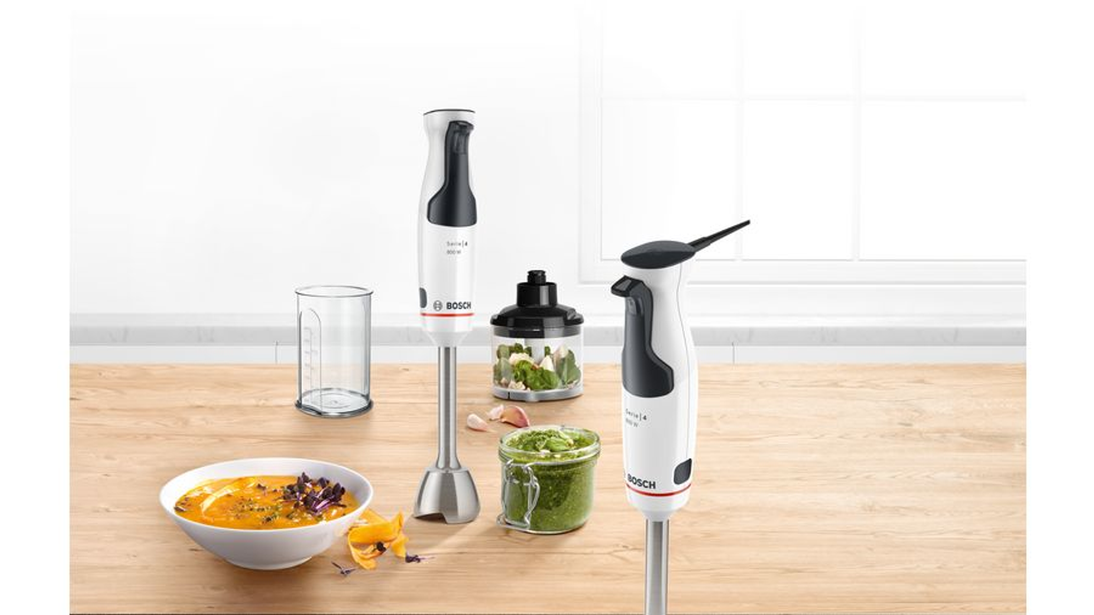Een tafel met een kom soep, een glas en een staafmixer. De mixer is wit en zwart.