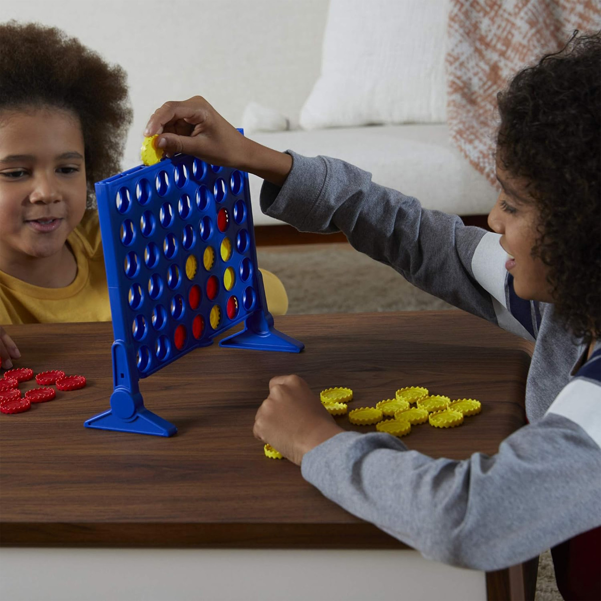 Kinder spielen das Spiel Connect Four auf einem braunen Tisch.