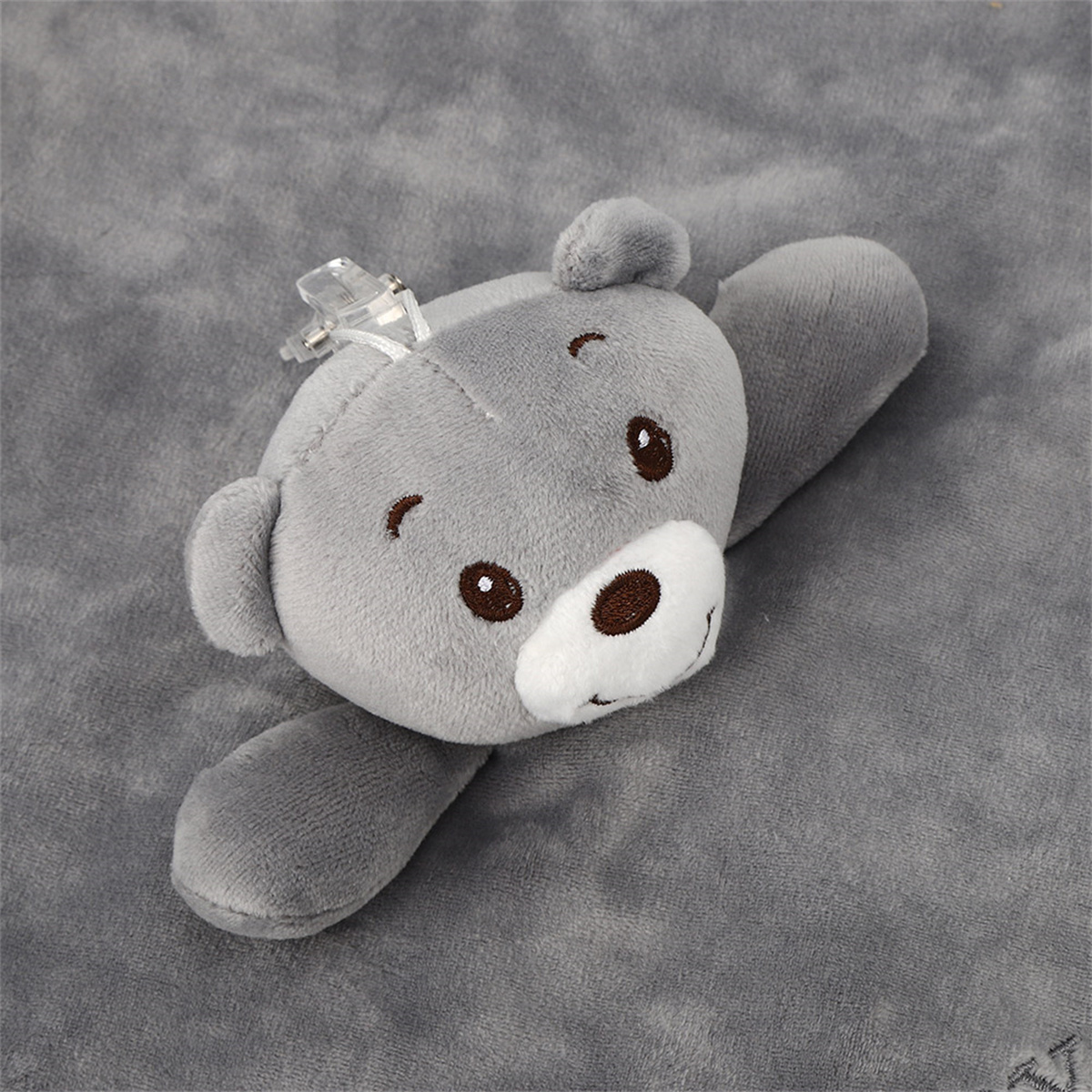 Ein graues Teddybär-Spielzeug mit einem klaren Ring. Der Bär liegt auf einer grauen Oberfläche.