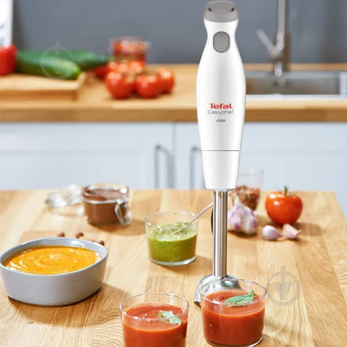 Witte Tefal EasyChef staafmixer op een houten tafel met voedsel eromheen.