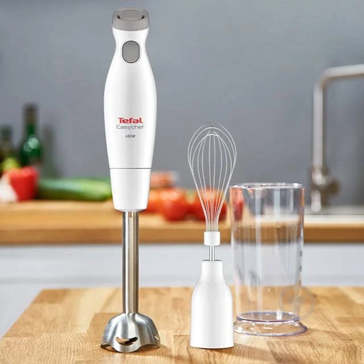 Witte en grijze staafmixer met garde en glazen beker op een houten aanrecht.