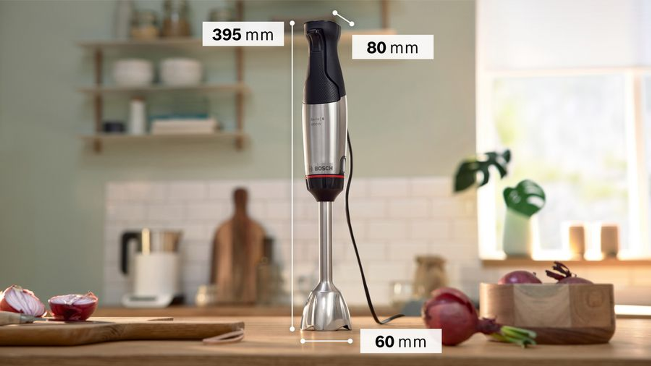 Un frullatore a immersione su un bancone di legno, con cipolle e altri oggetti.