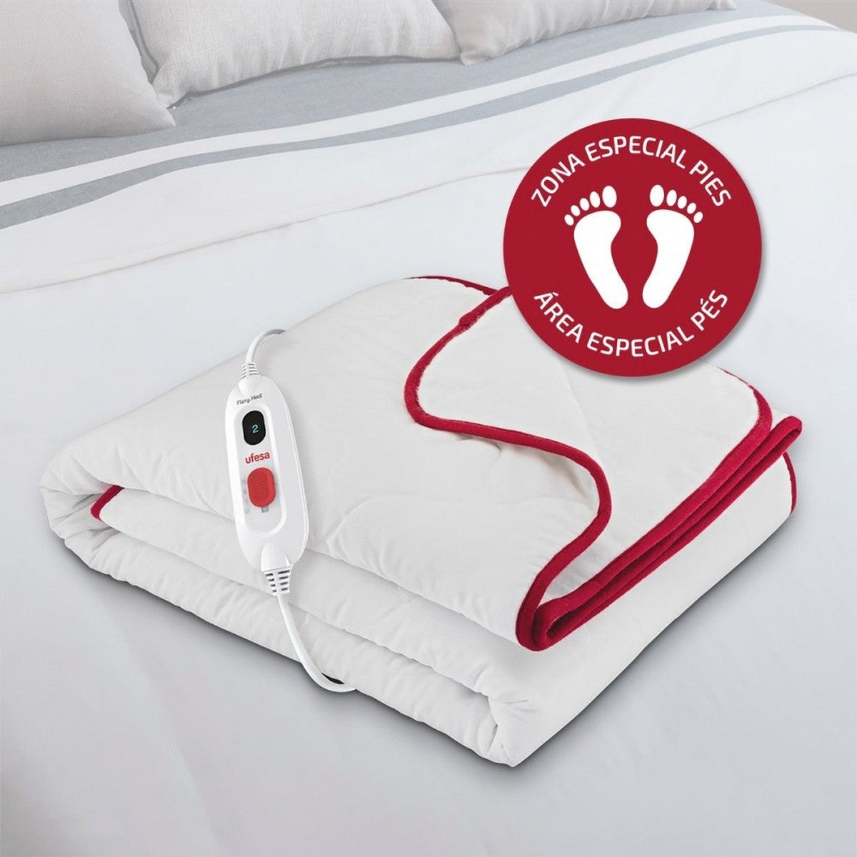 Una manta eléctrica blanca con ribete rojo, doblada sobre una cama. Un panel de control visible.