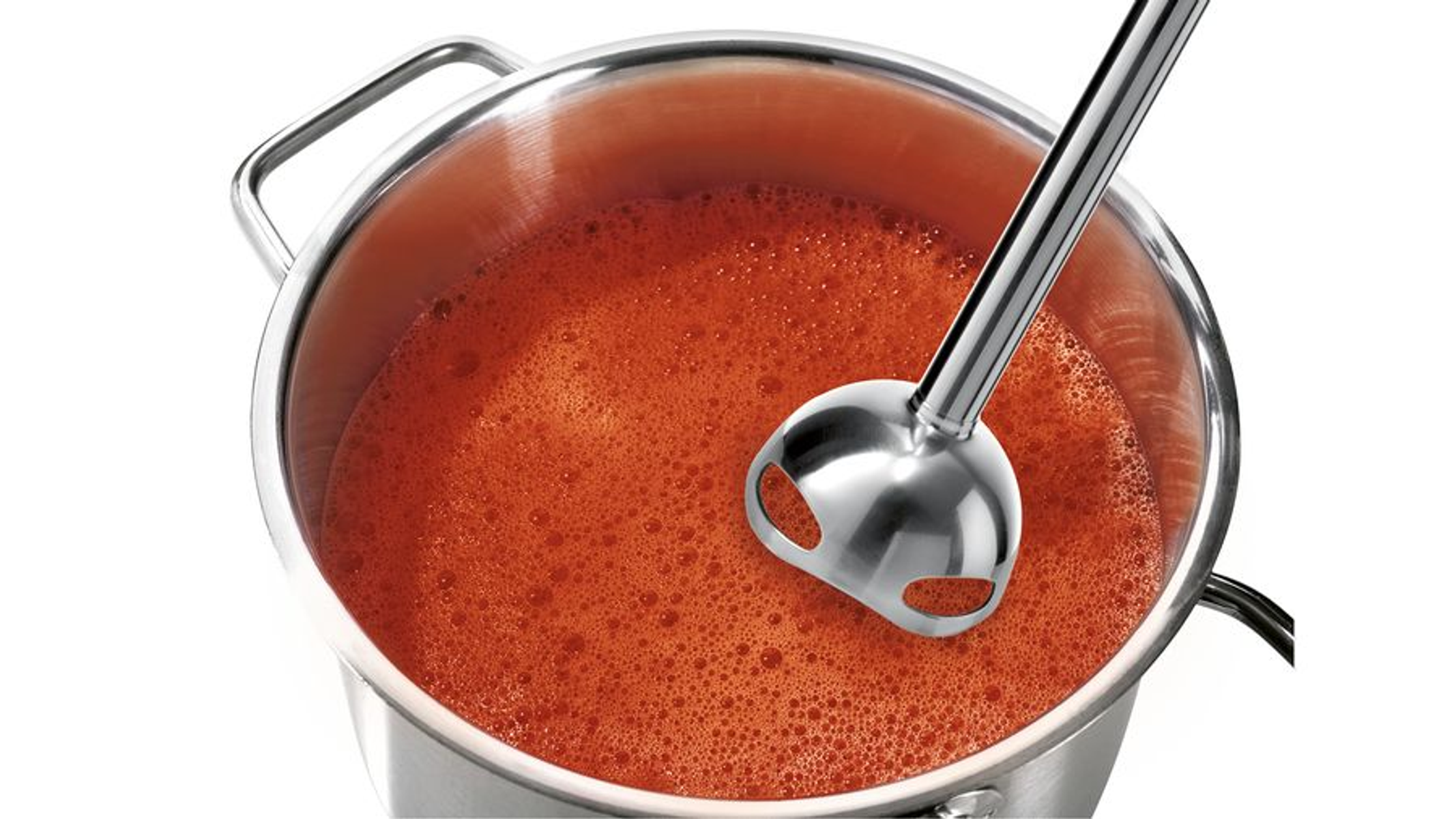 Srebrny blender w garnku z czerwoną zupą. Blender jest w zupie.