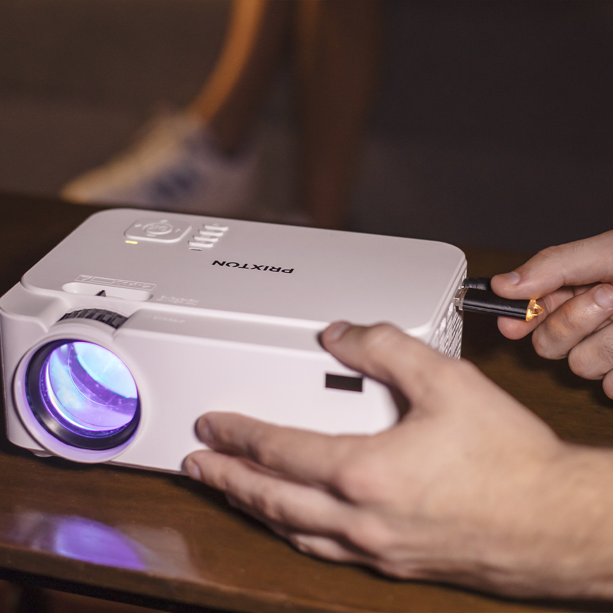 Biały projektor ze skupieniem na obiektywie, ręka wkładająca czarny kabel.