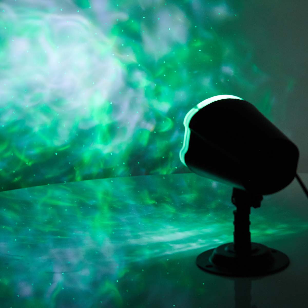 Ein schwarzer Projektor projiziert grüne und blaue Nebel auf eine Oberfläche.