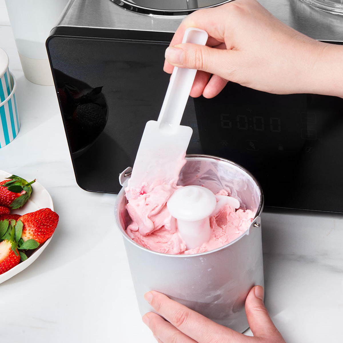 Eine Person schöpft rosa Eiscreme aus einem Metallbehälter.