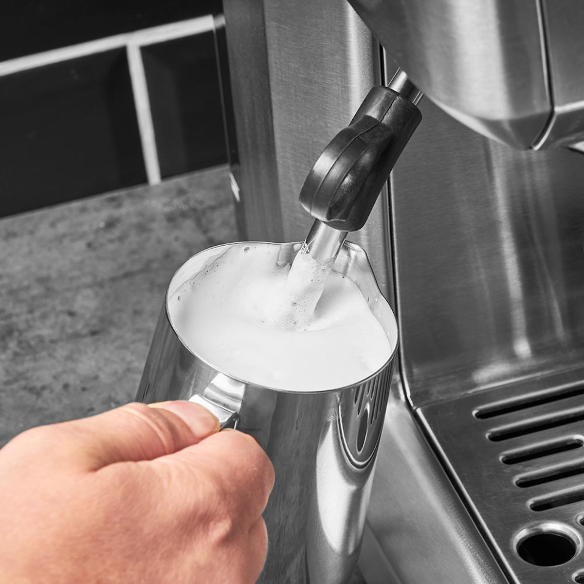 Para mleczna wlewana do metalowego dzbanka przez maszynę. Czarny uchwyt, stal nierdzewna.