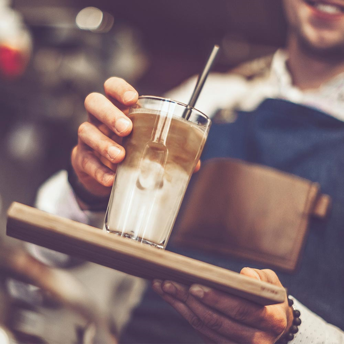 Osoba trzymająca szklankę warstwowego napoju kawowego na drewnianej tacy.