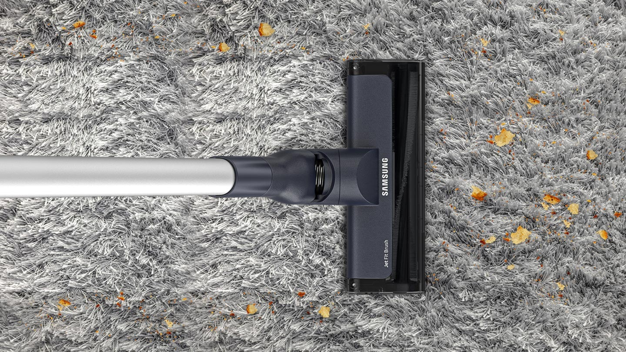 Odkurzacz czyszczący szary dywan. Głowica Samsung w kadrze. Rozrzucone beżowe zanieczyszczenia.