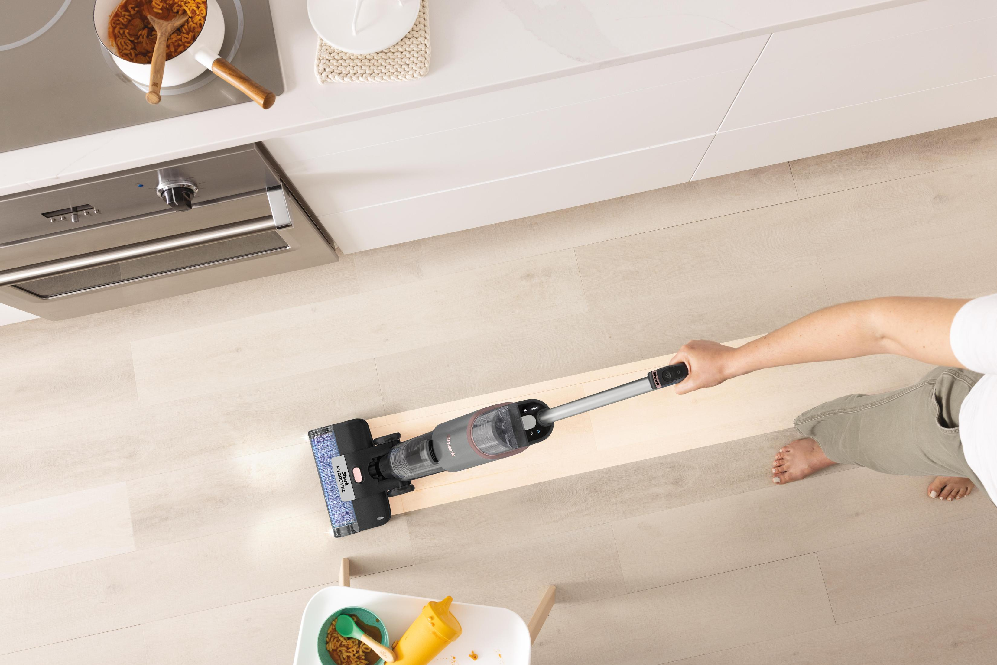 Person saugt einen hellen Holzboden mit einem kabellosen Staubsauger.