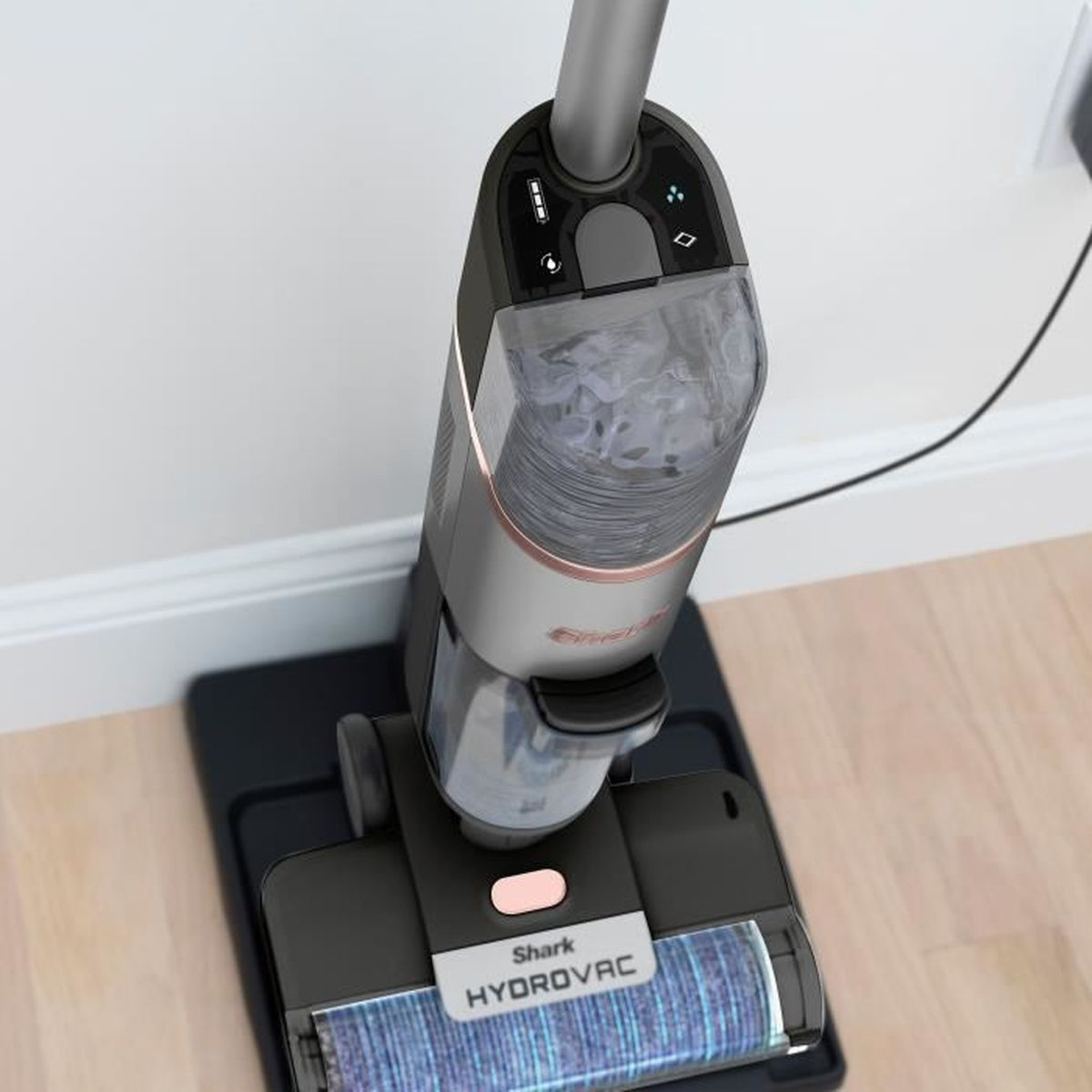 Aspirateur vertical sur une base de chargement. Gris et noir avec texte 'Shark Hydrovac'. Prise murale en arrière-plan.