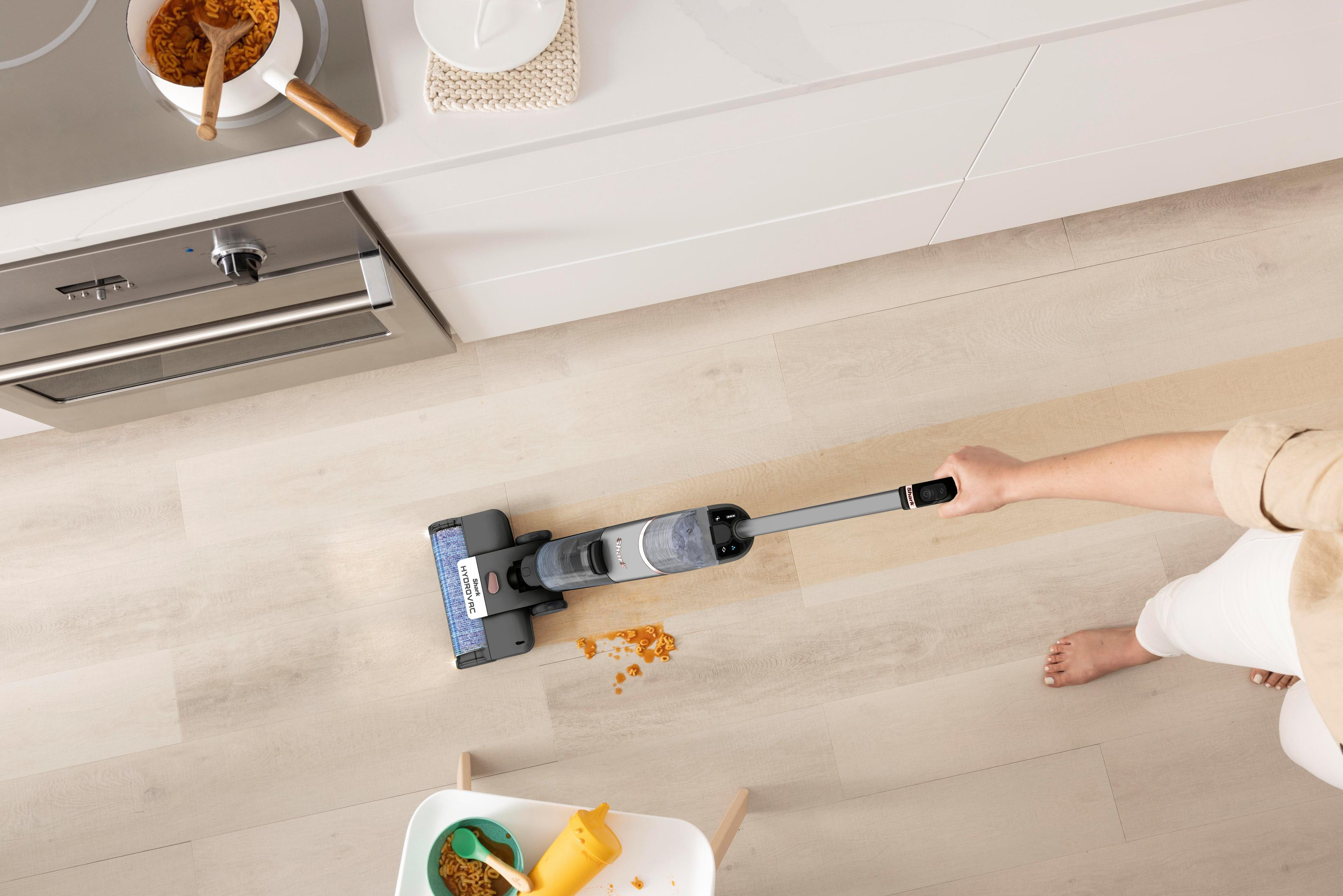 Une personne passant l'aspirateur sur un sol avec un appareil de nettoyage, près d'une cuisinière et de déversements de nourriture.