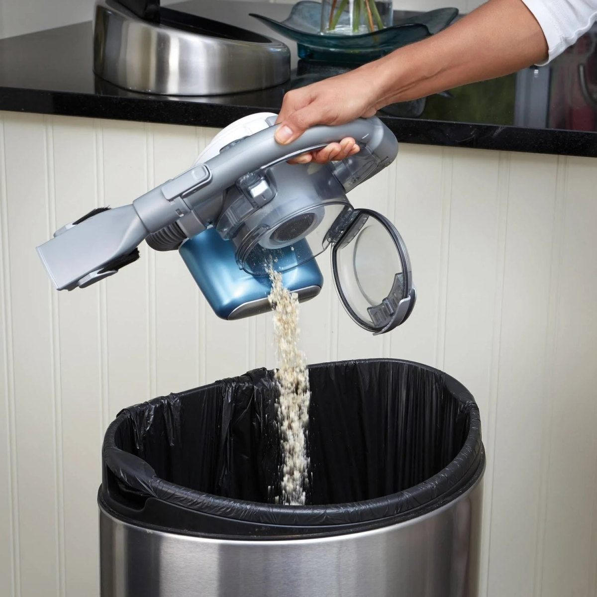 Une main vidant le contenu d'un aspirateur à main dans une poubelle.