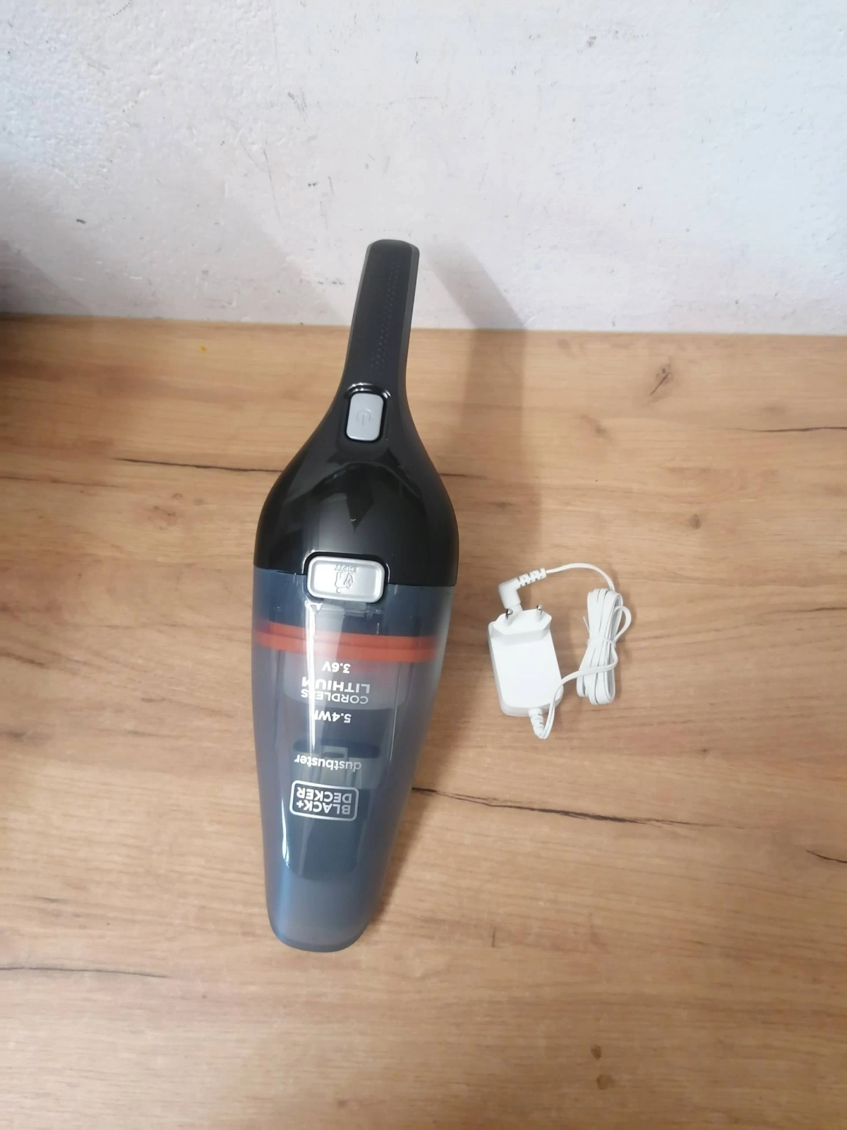 Aspirapolvere portatile nero e grigio con base di ricarica su una superficie di legno.