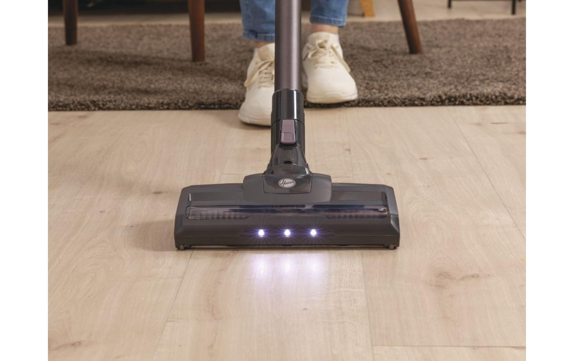 La testina di un aspirapolvere è su un pavimento di legno. Tre luci illuminano la superficie.