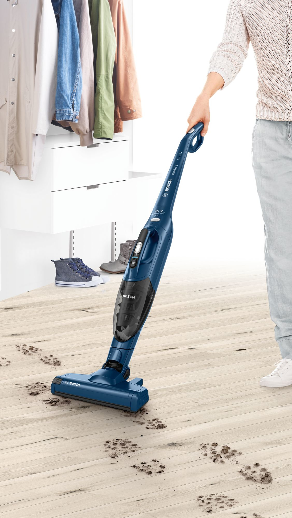Een persoon die een houten vloer stofzuigt, met een blauwe handstofzuiger en vuilsporen.
