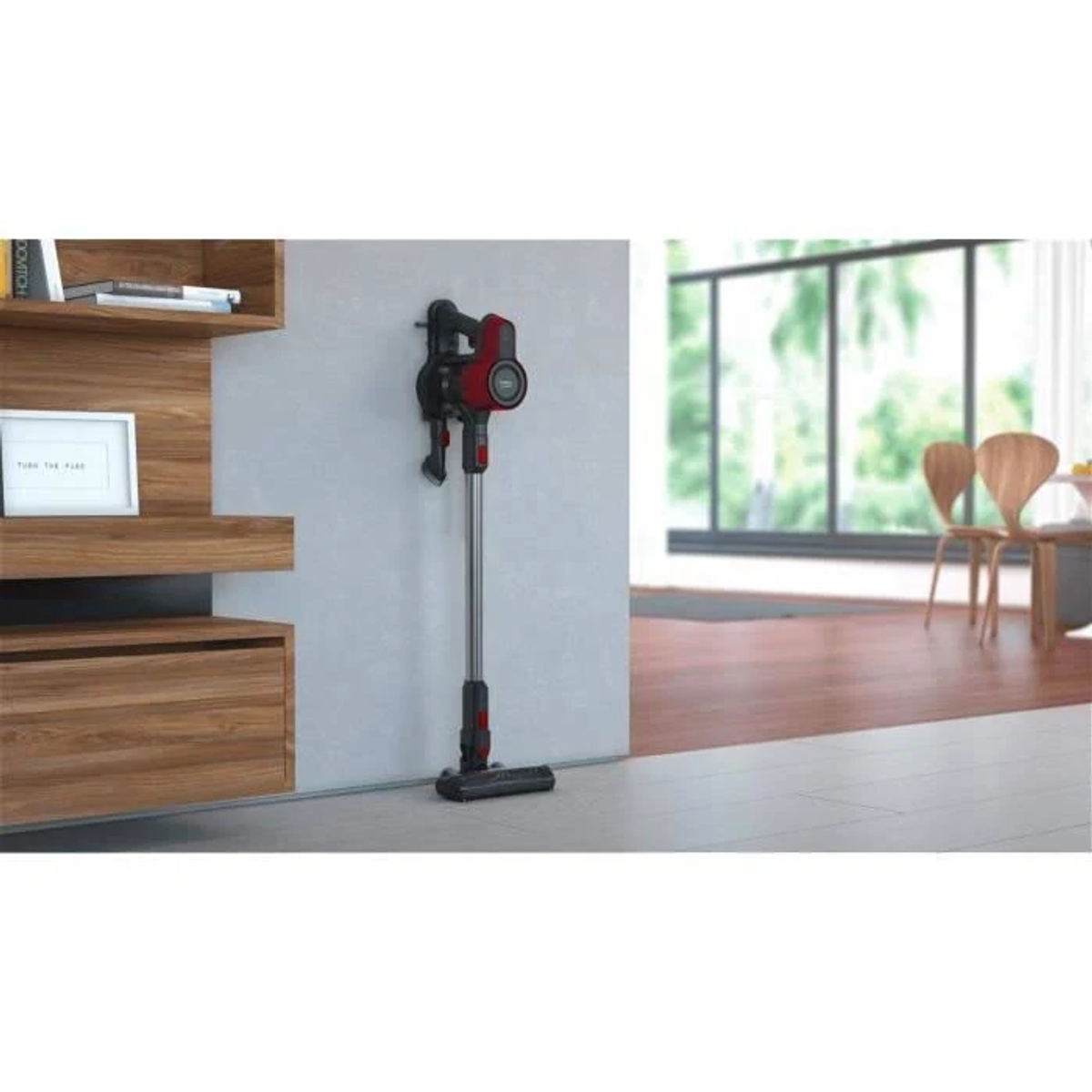 Ein rot-schwarzer Akku-Staubsauger an einer Wand, in der Nähe von Holzmöbeln.