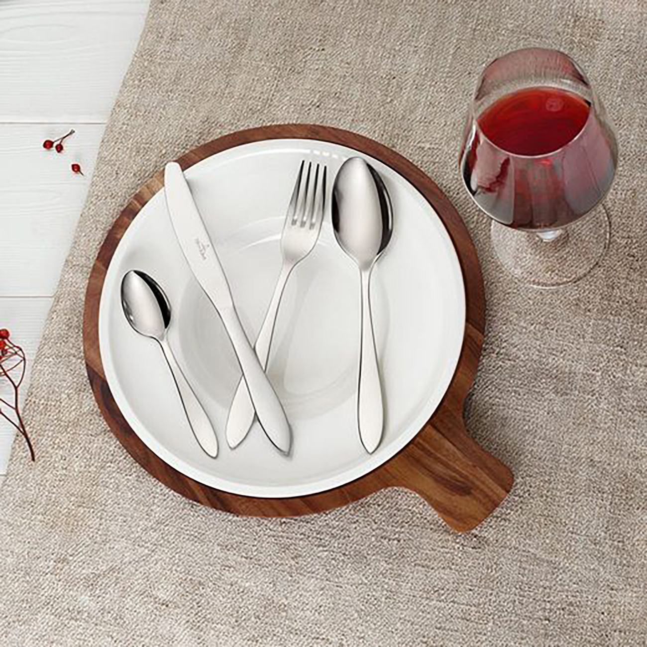 Tischarrangement mit Besteck auf Holztablett, Glas Rotwein. Beige Oberfläche.