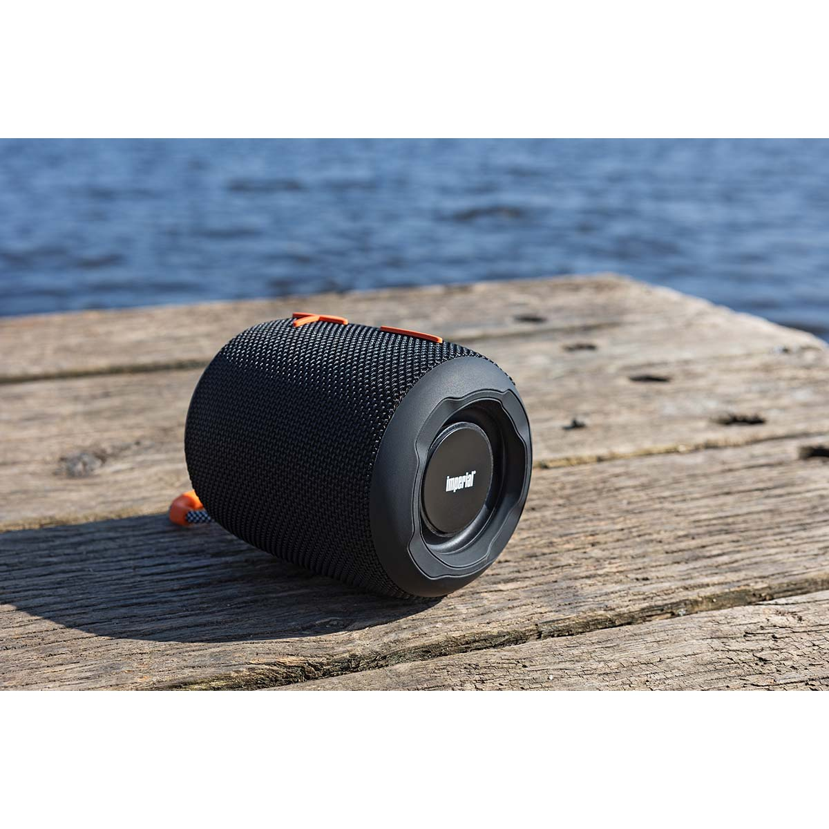 Een zwarte en oranje luidspreker op een houten steiger met water op de achtergrond.