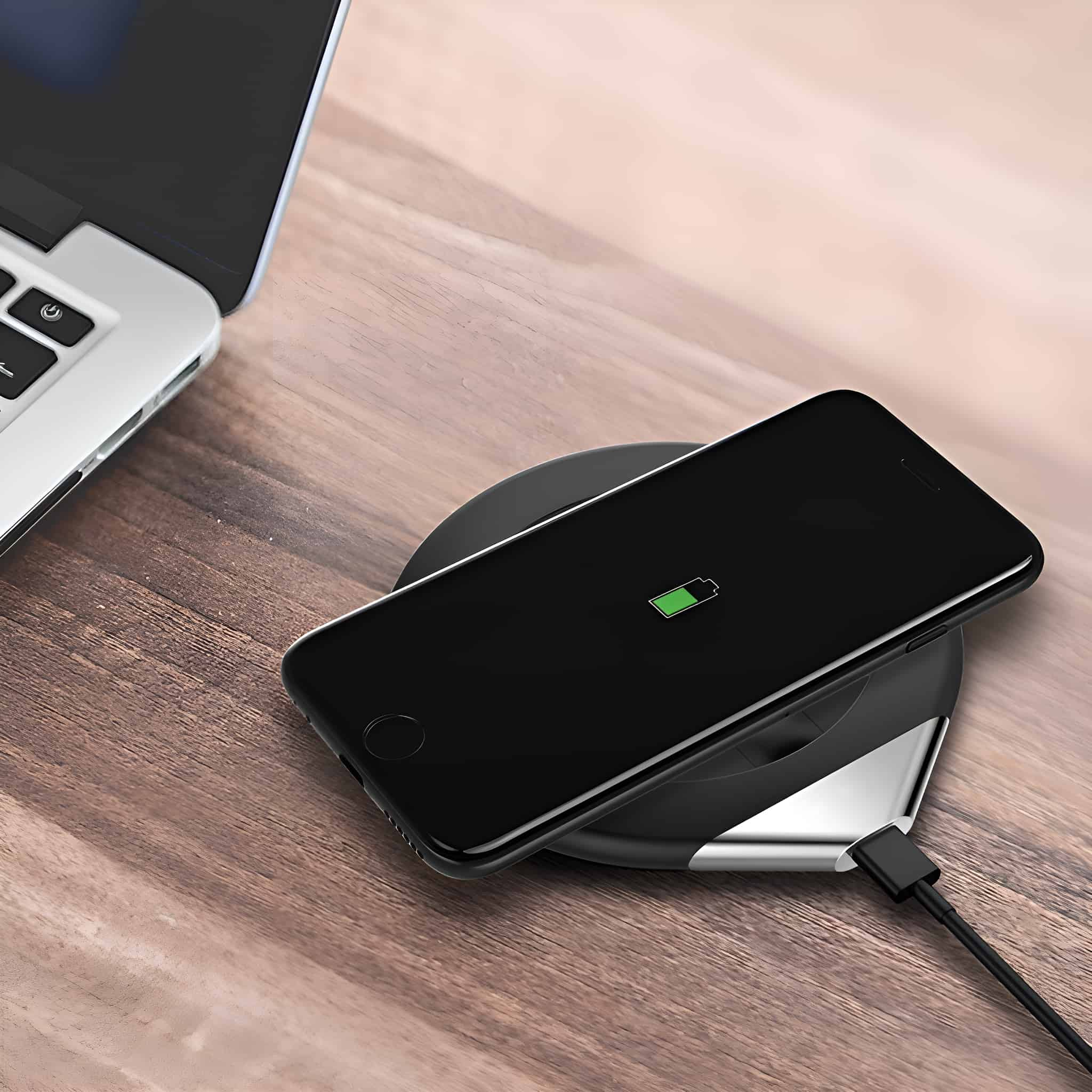 Schwarzes Telefon, das auf einem kabellosen Ladegerät auf einem Holztisch lädt.