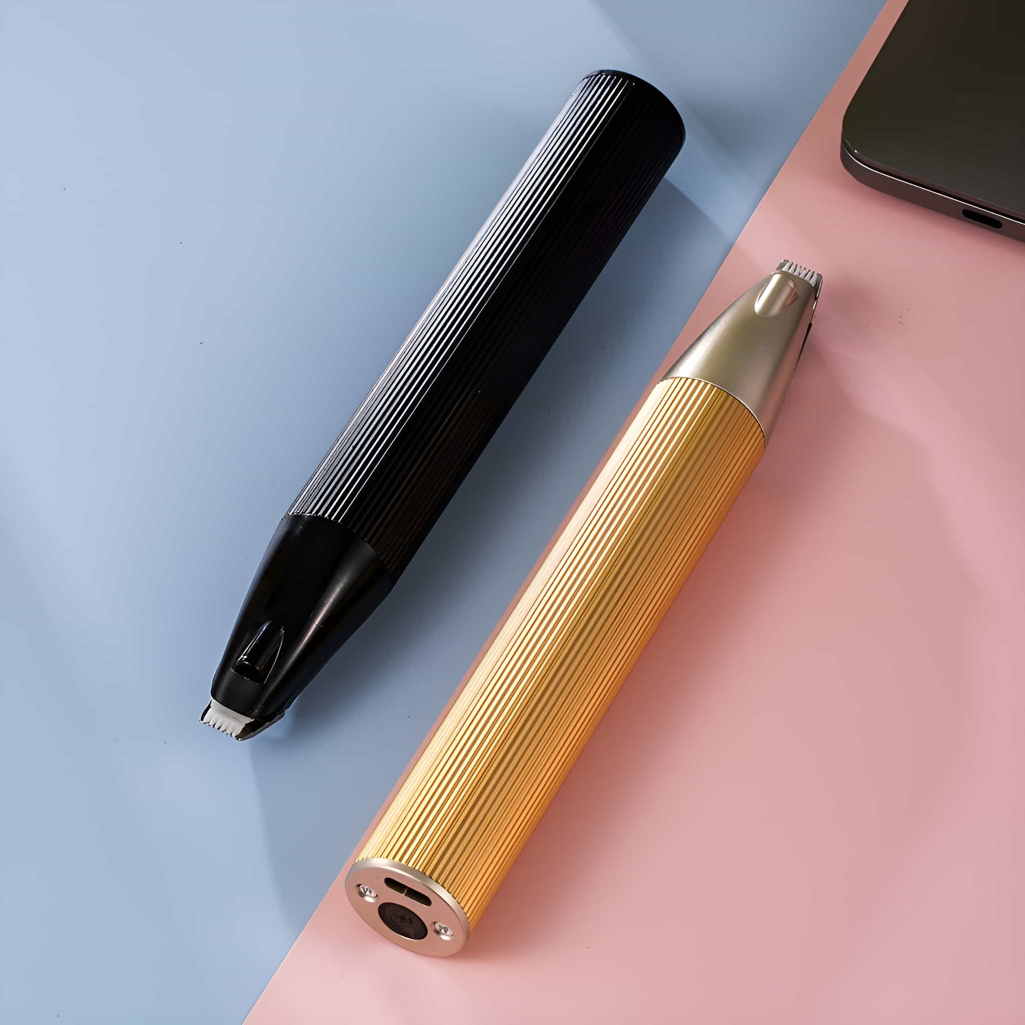 Zwei Nasenhaartrimmer, einer schwarz und einer gold, auf einer rosa und blauen Oberfläche. Beide haben Metalltrimmerköpfe.