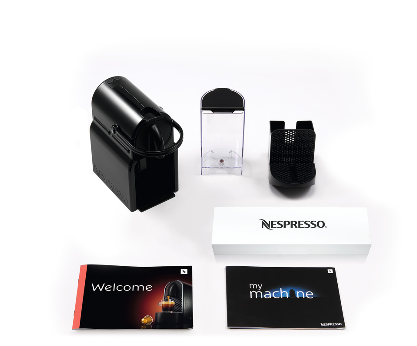 Czarny ekspres Nespresso, pojemnik na wodę, pojemnik na kapsułki, pudełko i dwie broszury. Białe tło.