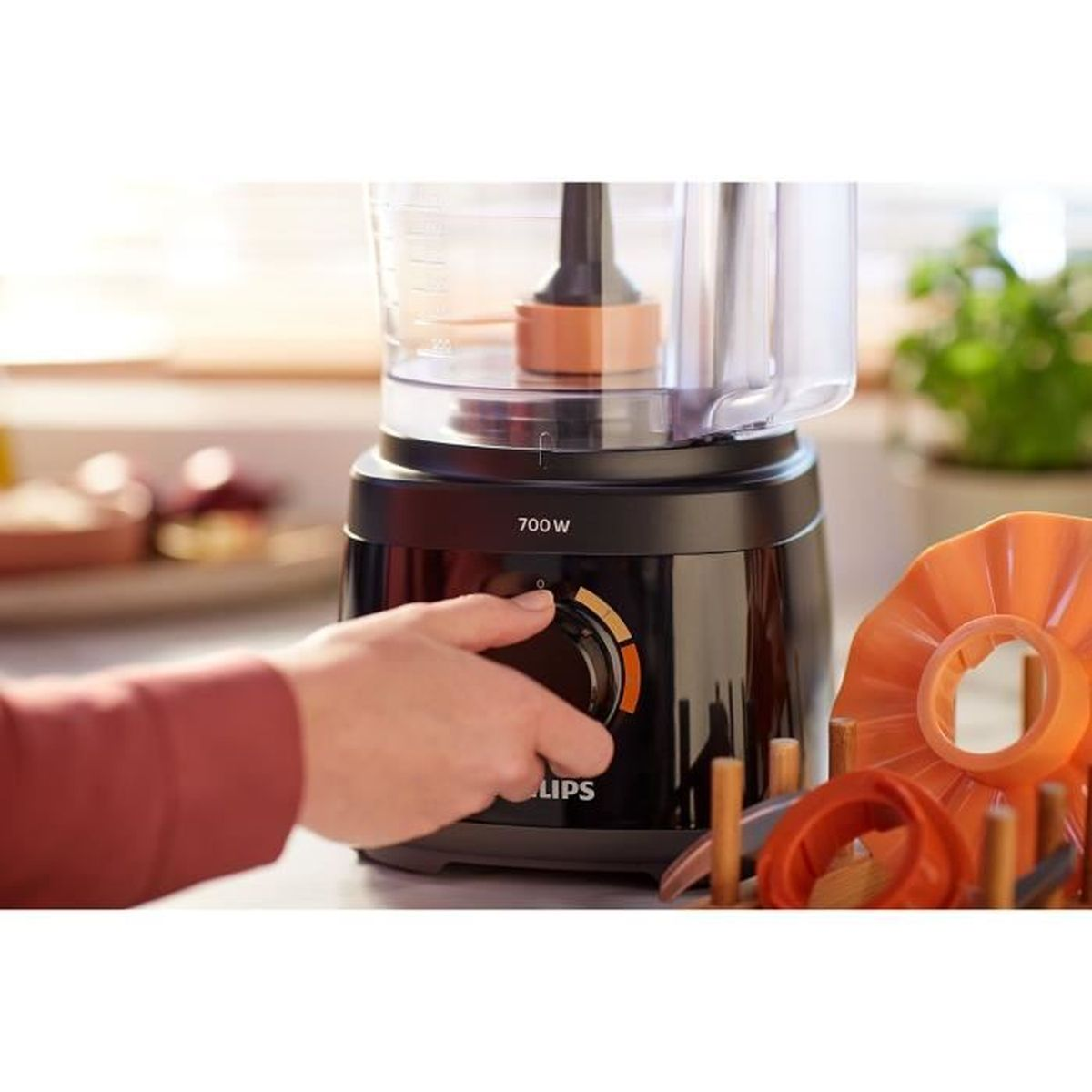Procesador de alimentos Philips negro con una mano girando una perilla. Se ven detalles naranjas y blancos.