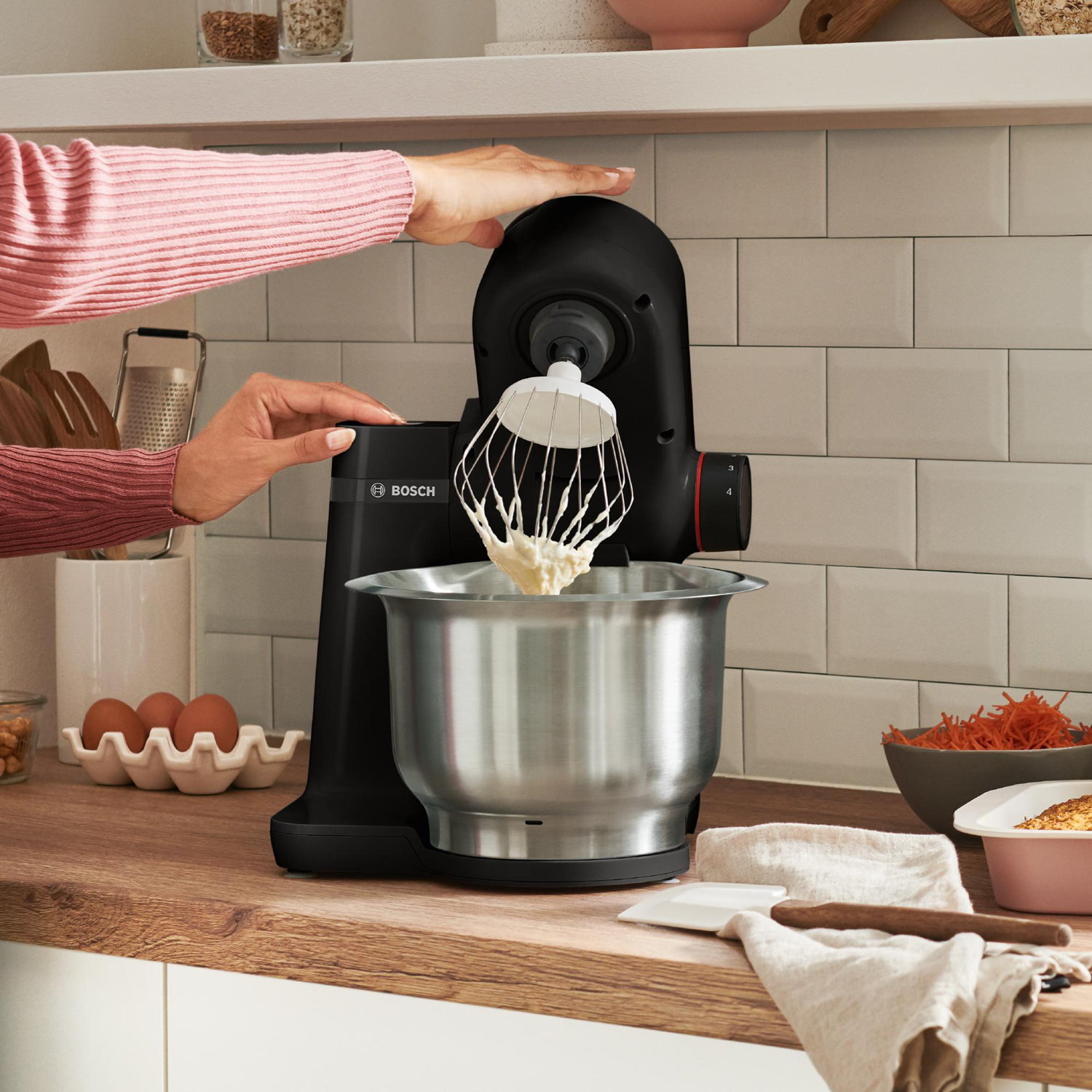 Eine Frau benutzt eine Küchenmaschine. Sie ist schwarz mit einer silbernen Schüssel und weißer Creme.