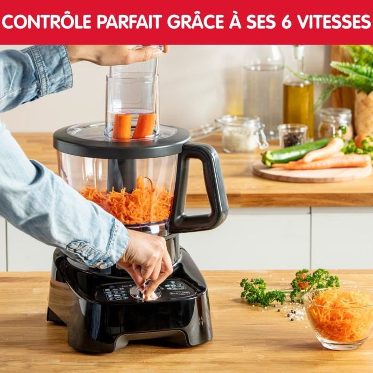 Un procesador de alimentos negro con zanahorias en proceso. Una mano opera la máquina.