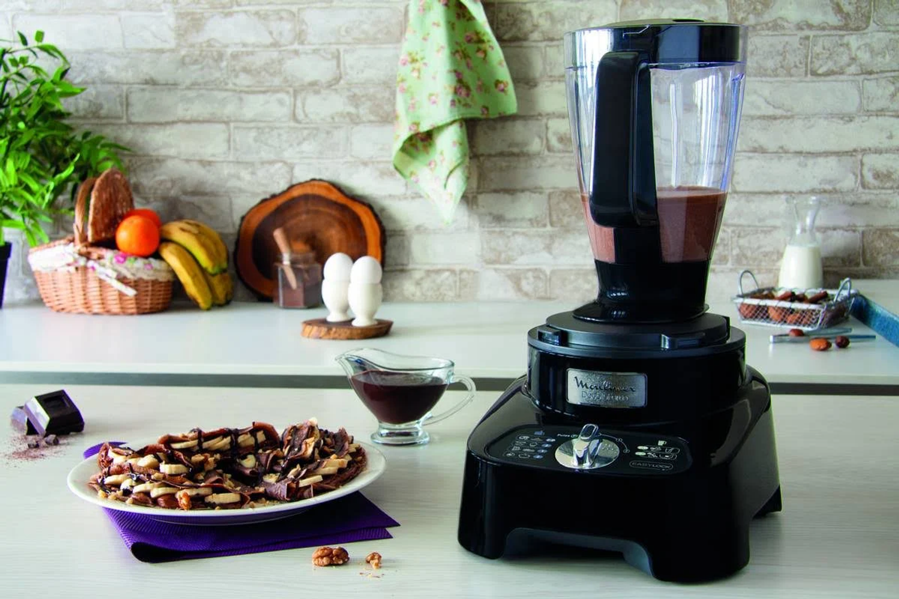 Licuadora negra con batido de chocolate, fruta y gofres en una encimera de cocina.